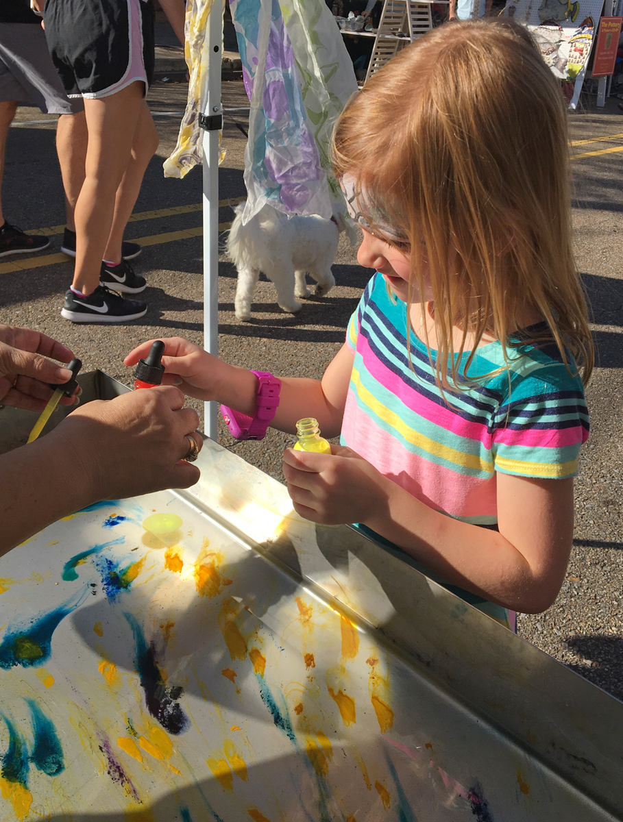 A young person hand dyes a silk scarf during the Holiday Festival of Arts.