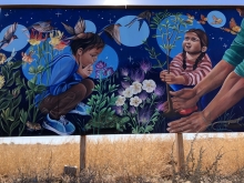 A painted mural featuring two children under a night sky among flowers, trees, birds, butterflies, and other fauna.