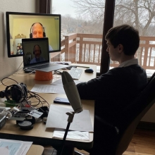 Sean Baker, a high school student, sits in front of two computer screens conducting a video interview with Randy Cohen of Americans for the Arts. 